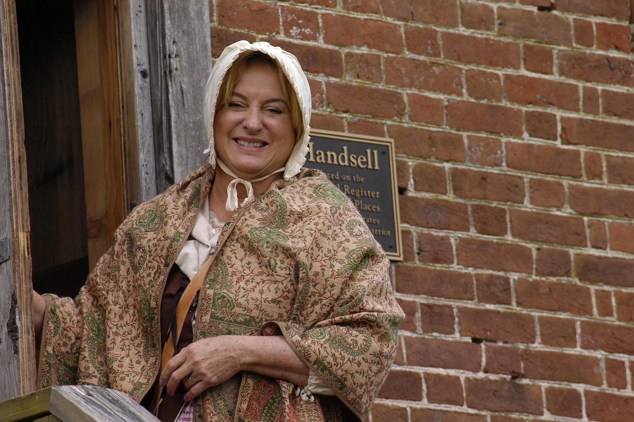 Midge in-character smiling out the front door of Handsell house.