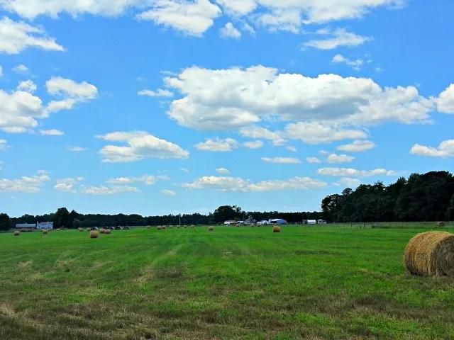 Beautiful blue sky with little puffy clouds, green green grass and bails of hay.